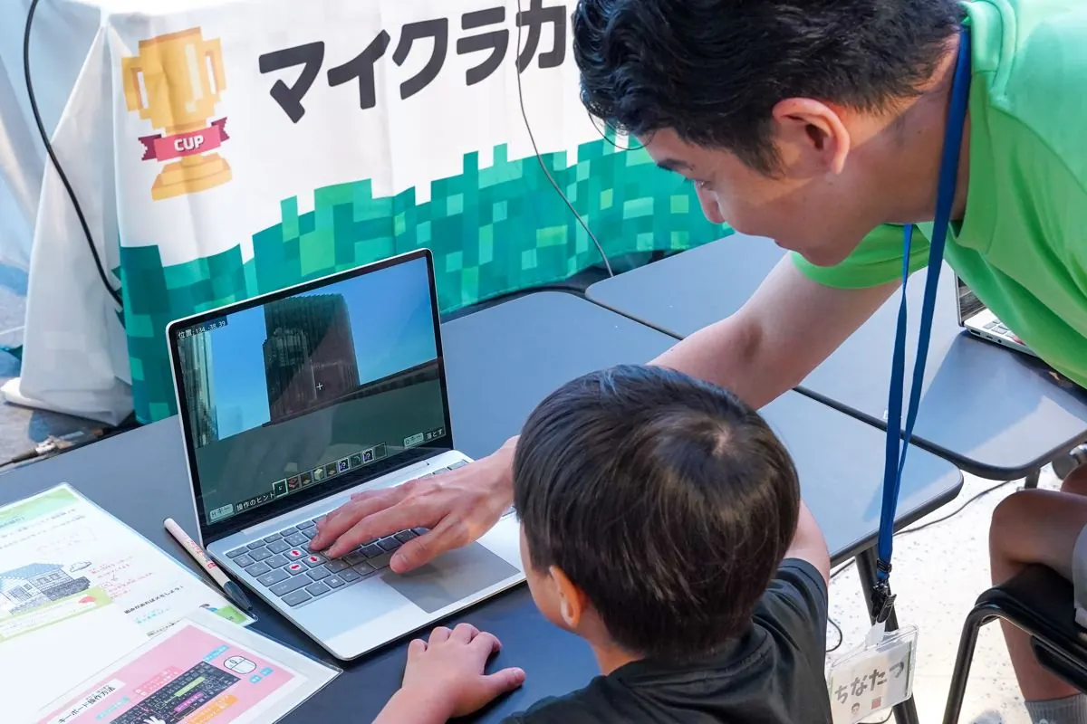 マイクラの画面を見ながら講師と一緒に操作を確認する子ども